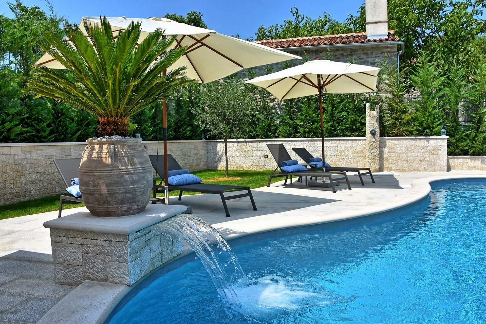 A swimming pool with a waterfall feature, lounge chairs, and umbrellas.
