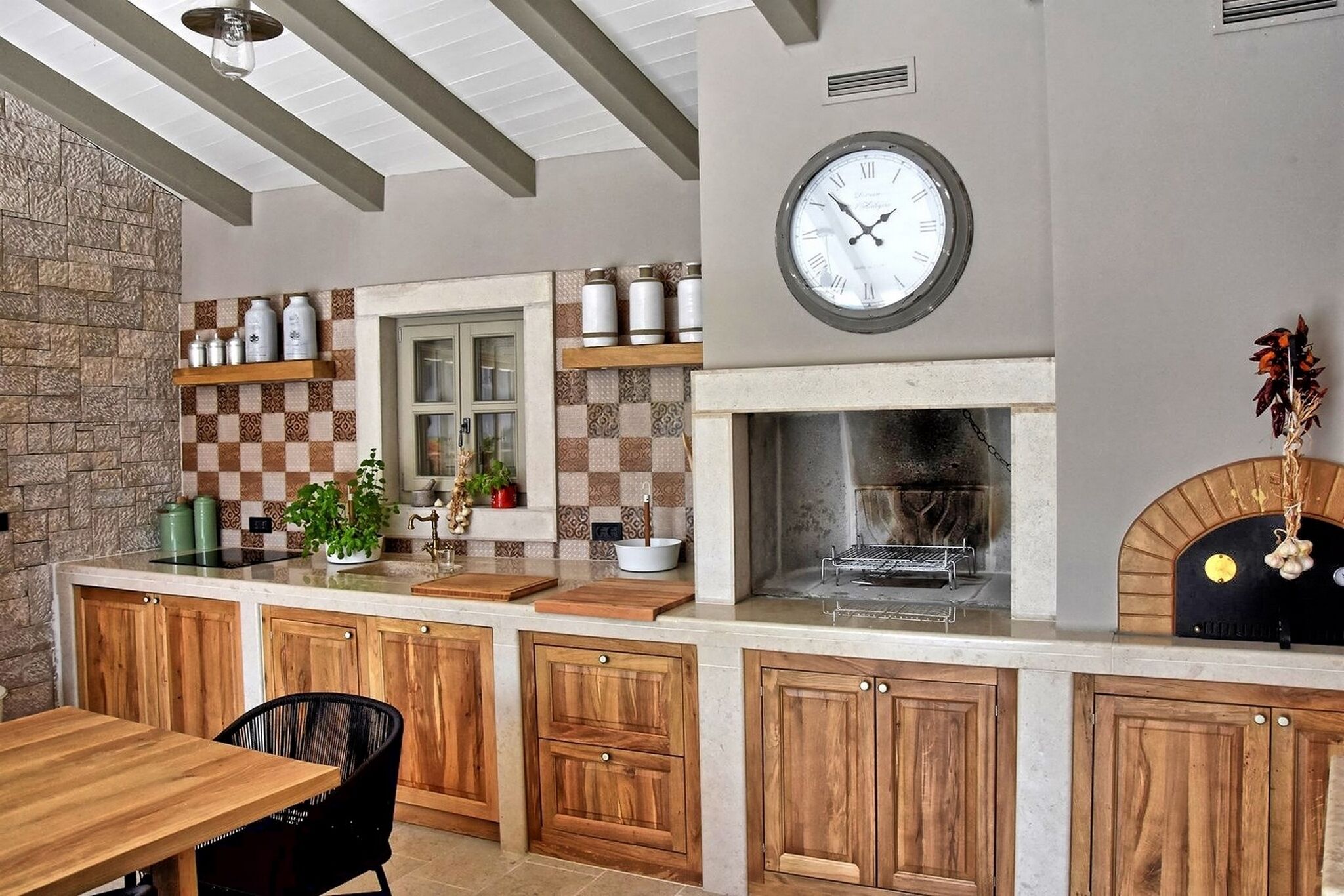 Een keuken met houten kastjes, een stenen muur, een geruit spatwand en een klok aan de wand.