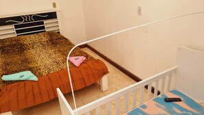 A bedroom with a bed, a small table, and a white railing. - Apartamento completo (Guaratingueta)