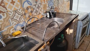 A kitchen with a stainless steel sink, a dish rack, a stove, and a gas cylinder. - Apartamento completo (Guaratingueta)