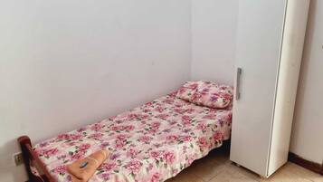 Una habitación pequeña con una cama individual, una colcha estampada, una silla de madera y un armario blanco.