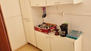 A small kitchenette with white cabinets, a coffee maker, a box of instant coffee, and a plastic container. - Apartamento completo (Guaratingueta)