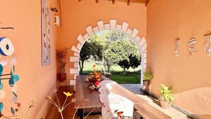 A covered outdoor seating area with a wooden table, potted plants, and a view of a garden.