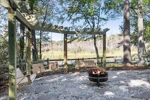 A wooden pergola with benches and a fire pit in a natural setting.