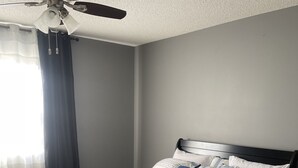 Ein ordentlich bezogenes Bett mit einer gestreiften Tagesdecke, einem blauen Kopfkissen und einem weißen Kopfkissen. Auf dem Bett liegt ein aufgerolltes Handtuch.