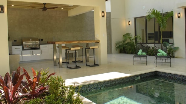 A modern outdoor kitchen with a pool, bar stools, and lounge chairs. - Perfectly located in Playa Guiones. Walk to the beach, shops, restaurants & yoga (Nosara)
