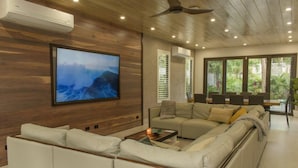 A modern living room with a large flat-screen TV, a sofa, a coffee table, and a ceiling fan. - Perfectly located in Playa Guiones. Walk to the beach, shops, restaurants & yoga (Nosara)