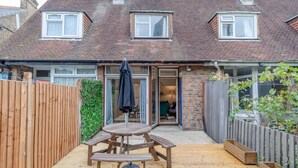 A wooden deck with a picnic table and chairs, a wooden fence, and a brick house with a sliding glass door. - Central 3 Bedroom House With Garden (London)