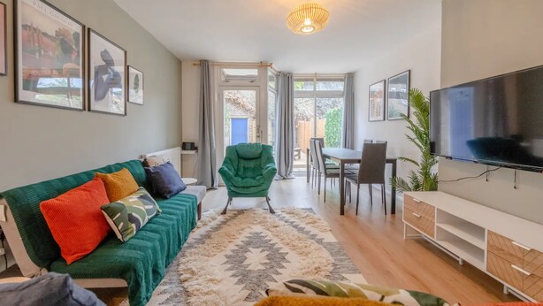 A modern living room with a green sofa, a large TV, and a dining area with a table and chairs. - Central 3 Bedroom House With Garden (London)