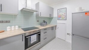 A modern kitchen with a built-in oven, a microwave, and a toaster on the countertop. There are cabinets with handles and a tiled backsplash. - Central 3 Bedroom House With Garden (London)