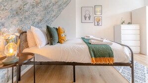 A bedroom with a bed, pillows, a bedside table with a lamp, a dresser, and wall art. - Central 3 Bedroom House With Garden (London)