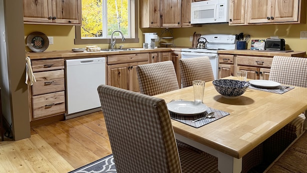 Una cocina con armarios de madera, lavavajillas, estufa y una mesa de comedor con sillas.