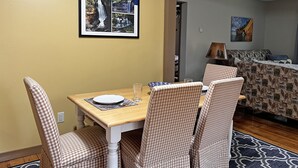 Un comedor con una mesa dispuesta para cuatro, sillas, un cuadro con una imagen de cascadas y una cama al fondo.