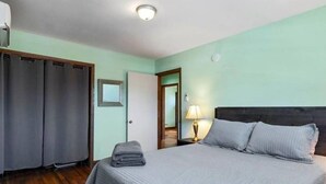 A bedroom with a bed, a nightstand, a lamp, a door, and a window.