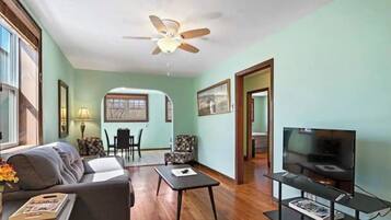 A living room with a sofa, coffee table, TV, and a ceiling fan.