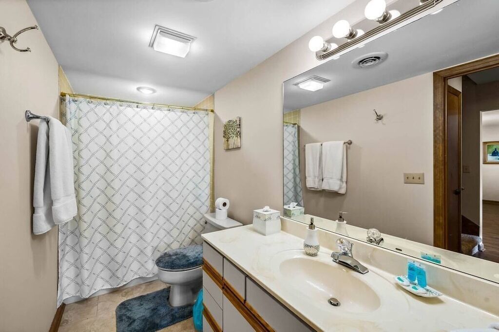 A bathroom with a shower curtain, a sink, a mirror, and a toilet.