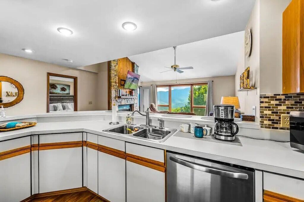 A modern kitchen with a corner island, stainless steel appliances, and a view of the outdoors.