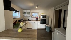 Une cuisine compacte avec des meubles blancs, un four à micro-ondes, un four et un lave-vaisselle. Il y a une petite fenêtre et un vase avec des fleurs sur le plan de travail.