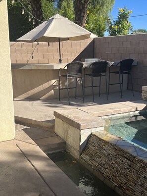 An outdoor patio with a pool, stone steps, and a barbecue area.