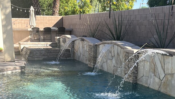 A clear pool with multiple water features, including a waterfall and a small fountain.