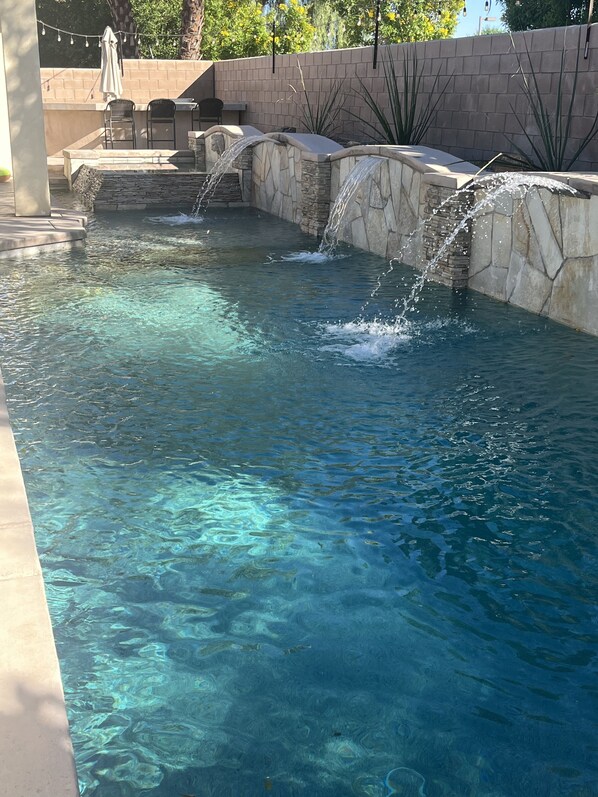 A clear pool with multiple water features, including a waterfall and a small fountain.