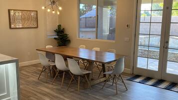 Un coin repas avec une table en bois et des chaises blanches, un lustre et une vue à travers une porte vitrée.