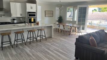 Une cuisine moderne avec des meubles blancs, un îlot central doté de tabourets et un coin repas avec une table et des chaises.