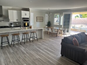 A modern kitchen with white cabinets, a central island with stools, and a dining area with a table and chairs.
