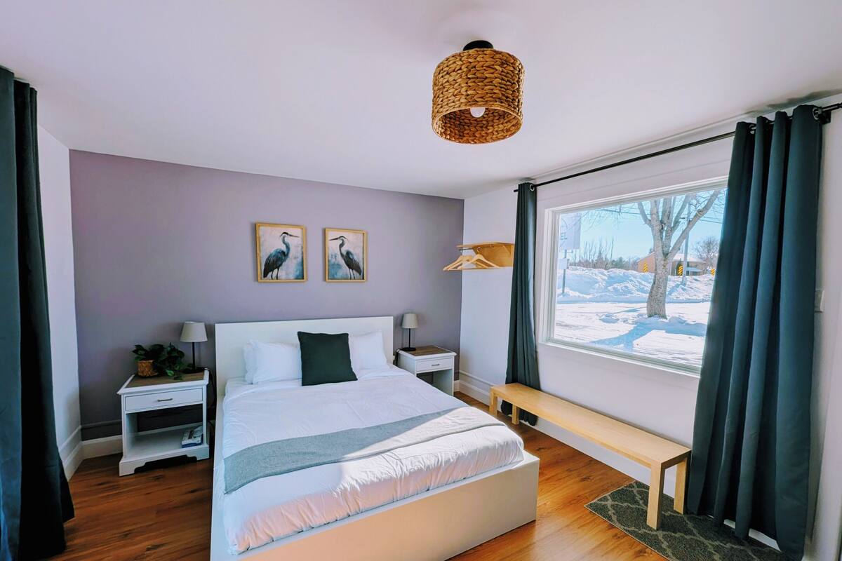 A modern bedroom with a large bed, bedside tables, a bench, and a window with a view of a snowy landscape.