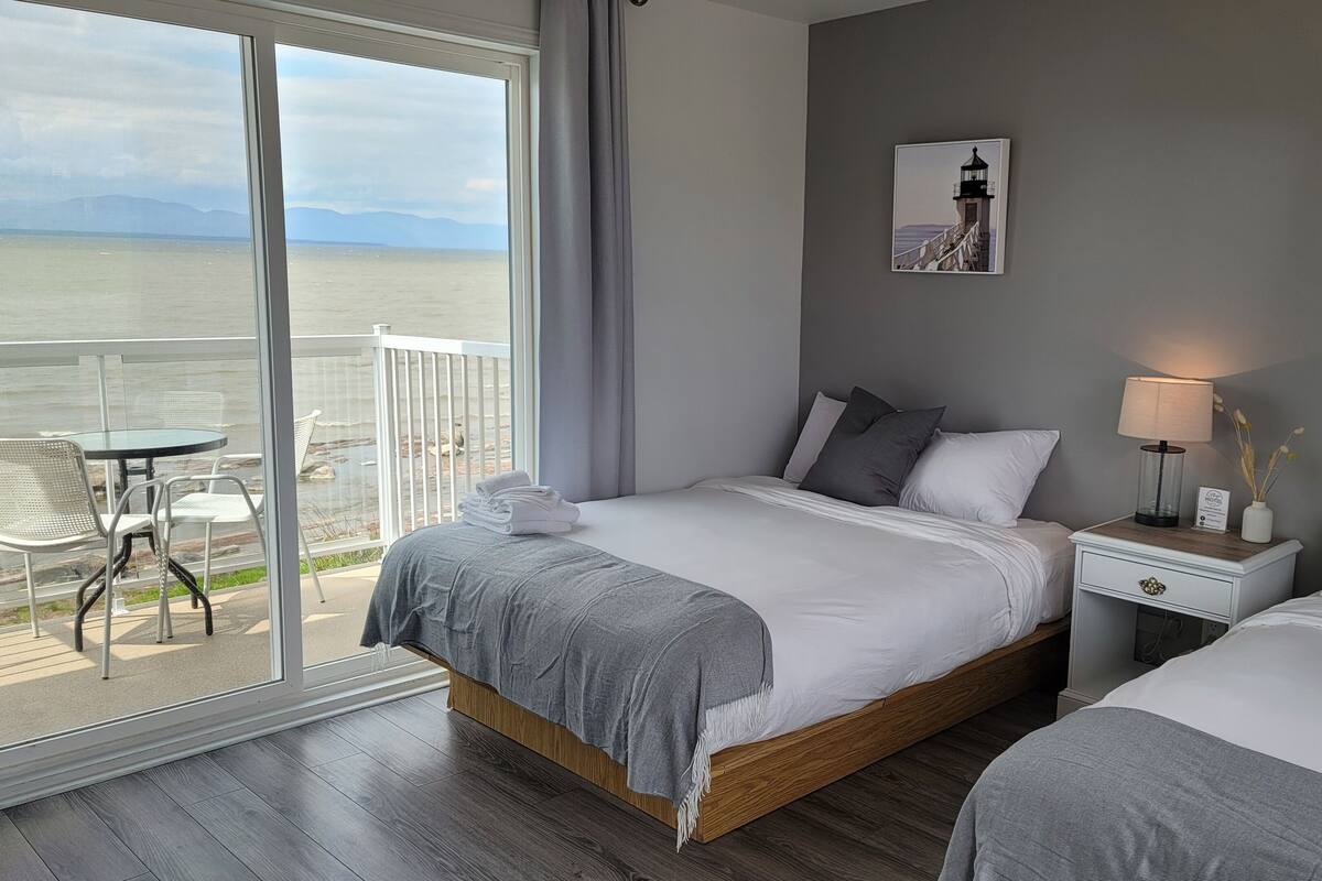 A hotel room with two beds, a balcony with a table and chairs, and a view of the sea.