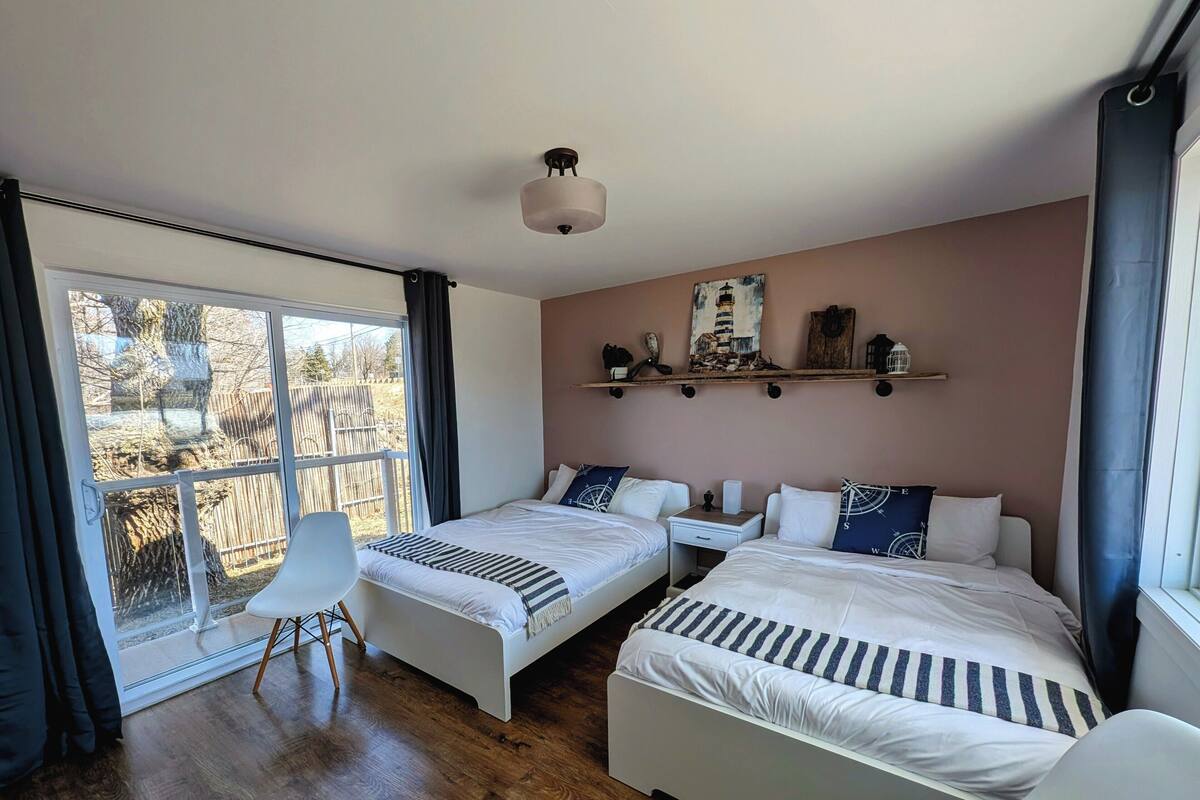 A bedroom with two beds, a desk, a chair, a window with curtains, and a ceiling light.