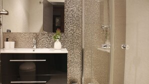 A modern bathroom with a glass shower enclosure, a white sink with a vase of flowers, and a dark vanity.