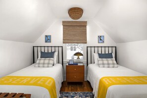 A bedroom with two beds, a wooden floor, a window with a view, a bedside table with a lamp, and a wall clock. - #15 Dog-Friendly 2BR Ocean-Block Cottage with Private Drive in Rehoboth Beach (Rehoboth Beach)