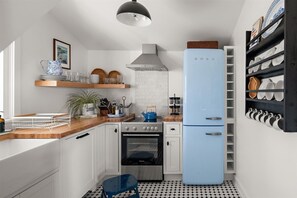 Cozinha compacta com armários brancos, geladeira azul, fogão a gás e um escorredor de louça suspenso.
