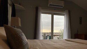 A hotel room with a large bed, a window with curtains, an air conditioning unit, and a view of a bridge and greenery outside. - * *Oceanfront | Hampton Beach | Pet Friendly* * (Hampton)