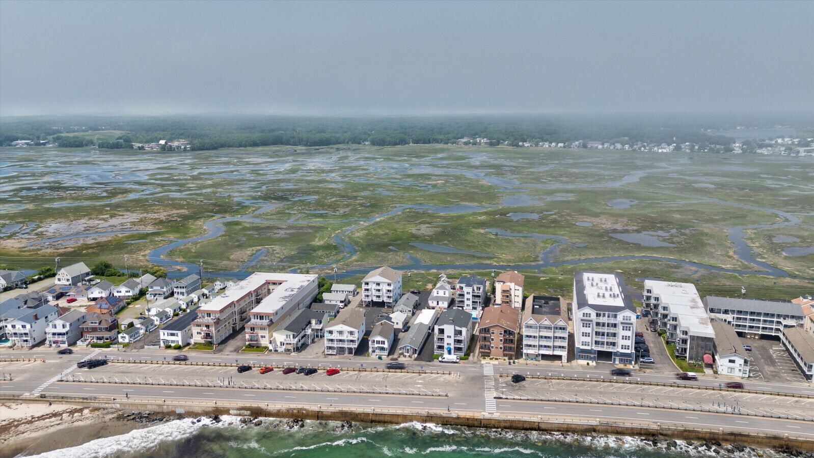 Vue aérienne d’une ville côtière avec un port de plaisance, des immeubles résidentiels et une route menant à la mer.