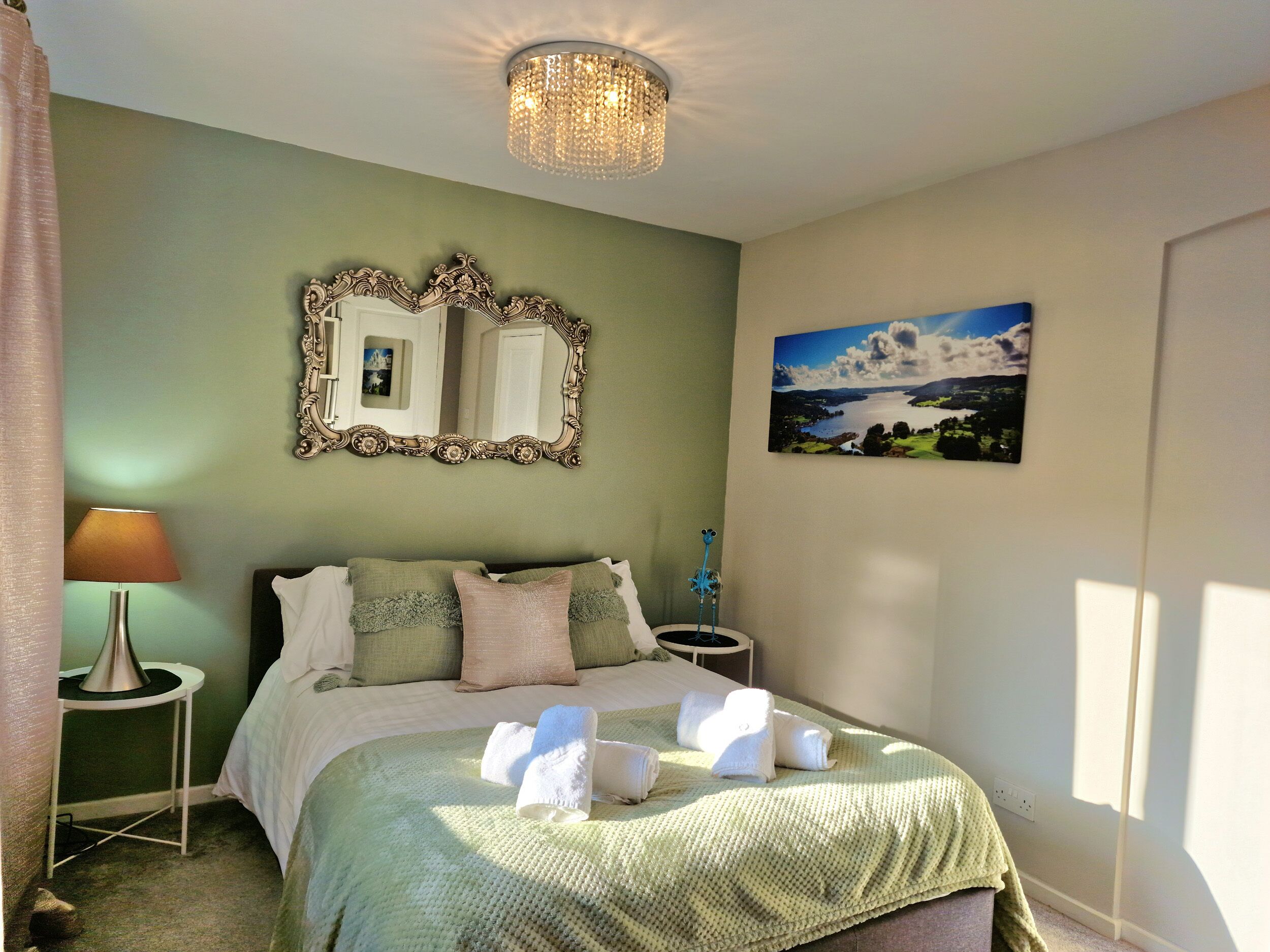 Un dormitorio ordenado con una cama, un espejo, una lámpara y un cuadro en la pared.
