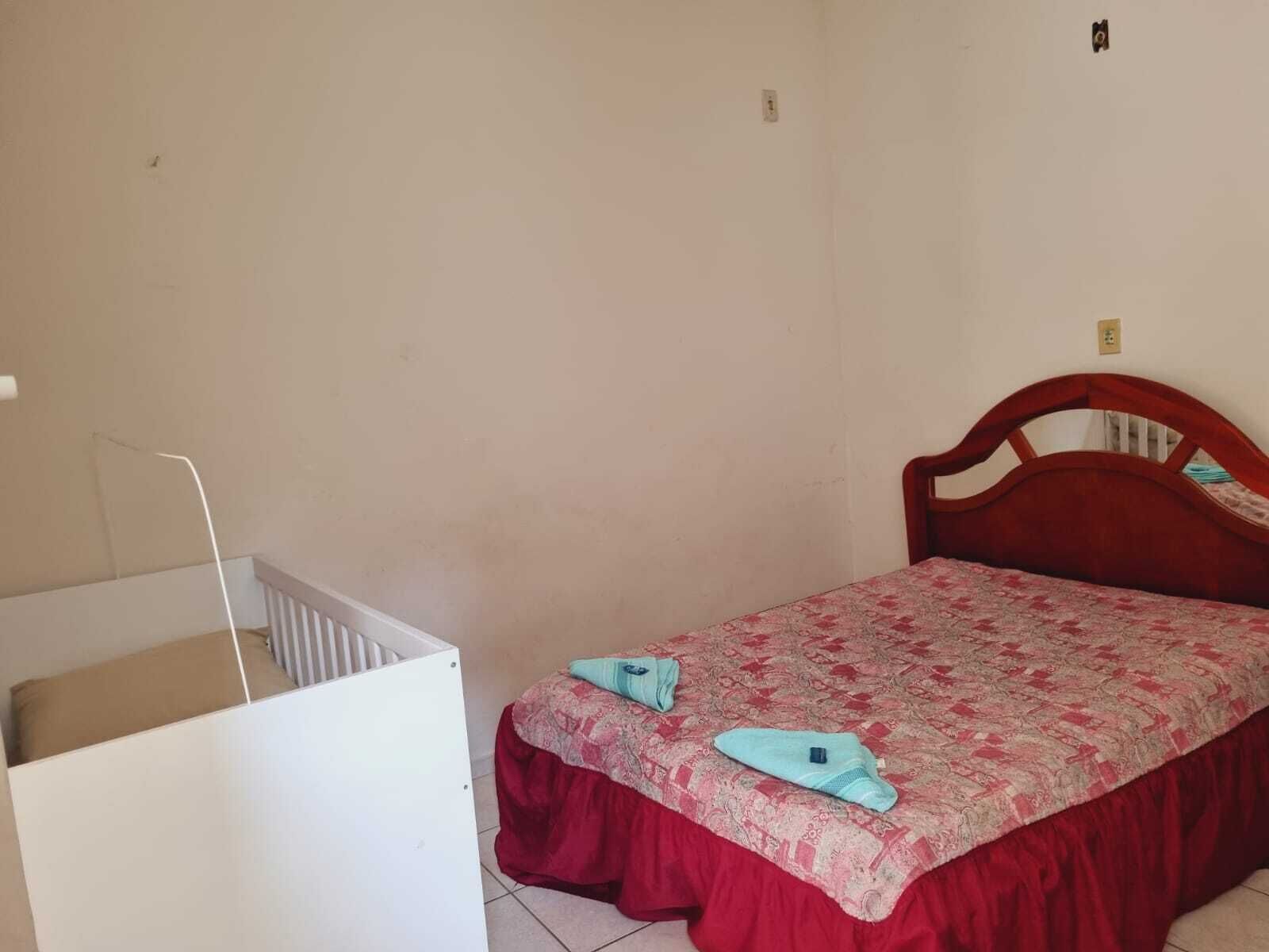 Habitació petita amb un llit individual, un capçal de fusta, una colcha vermella i una bressol blanca a la cantonada.