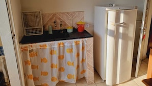 Una cocina pequeña con encimera negra, refrigerador blanco y cortina con estampado de peces.