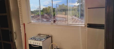 Una cocina con estufa a gas, un cilindro de gas y ventana con vista a una zona residencial.