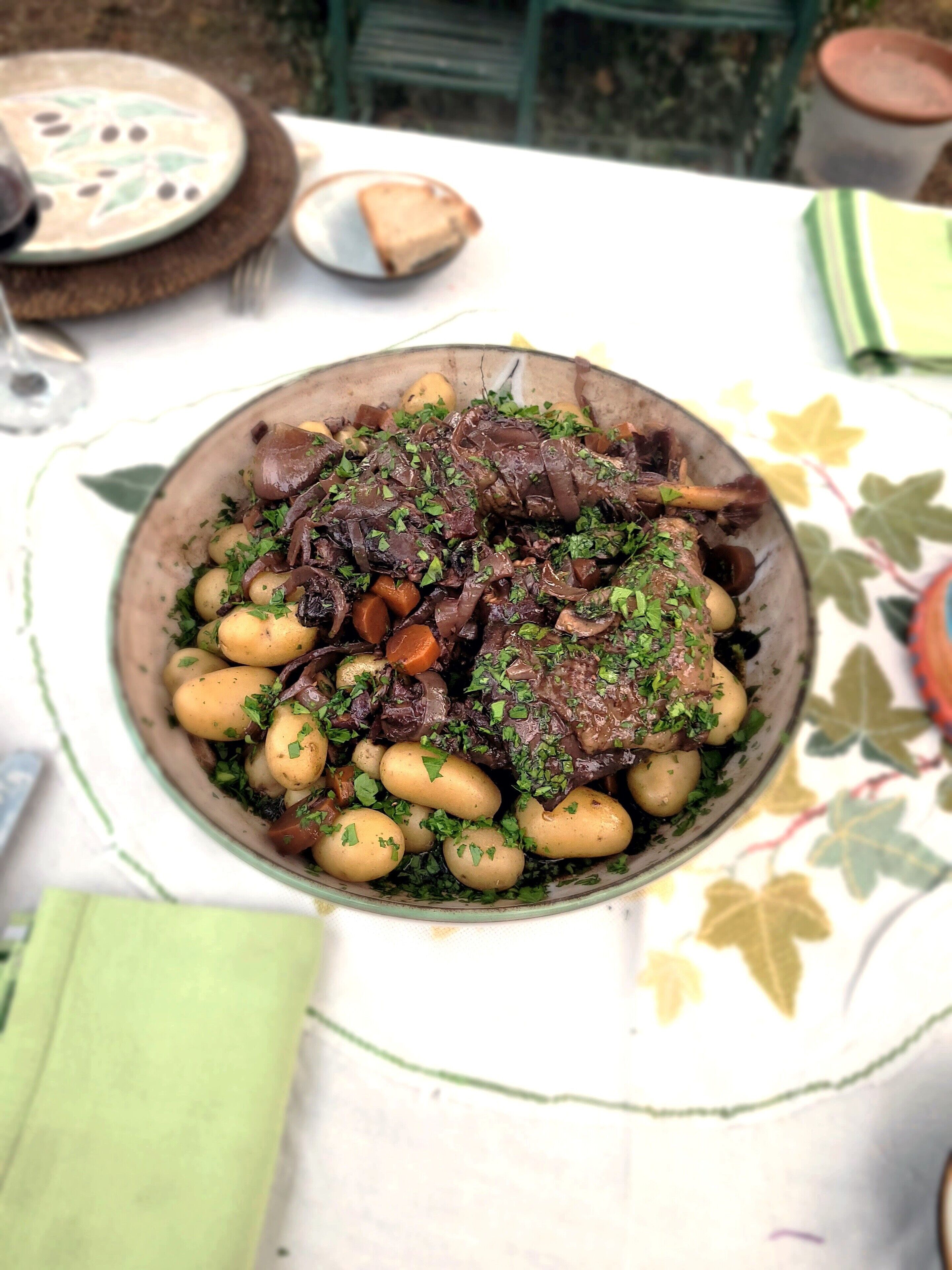 A large bowl of stew with meat and potatoes, served on a table with a floral tablecloth.