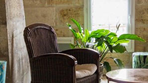 A rustic room with a stone wall, a wicker chair, a round table, and a large window. - La Ferme du Ciel (Laruscade)