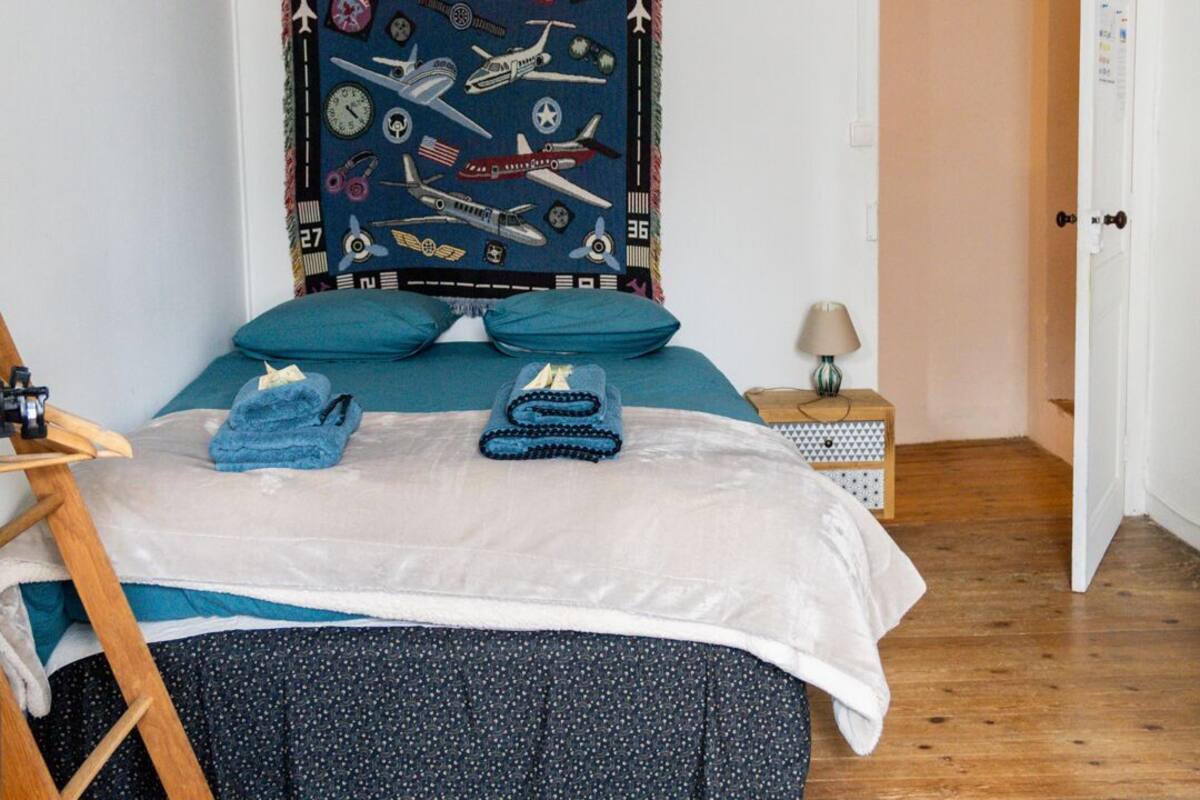 A bedroom with a bed, a wooden ladder, a small bedside table, a lamp, and a door.