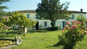 A traditional stone building with a tiled roof, surrounded by a well-maintained garden with flowering plants and a pond with lily pads. - La Ferme du Ciel (Laruscade)