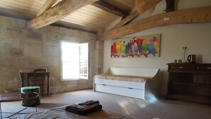 A room with a stone wall, wooden beams, a white bed, a painting of colorful parrots, a green chair, and a wooden cabinet. - La Ferme du Ciel (Laruscade)
