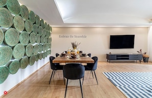 Enjoy meals in this stylish dining area with a wooden table and comfortable seating for four, accompanied by a unique green wall installation and a flat-screen TV.