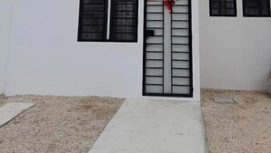 Ein modernes, zweistöckiges Gebäude mit flachem Dach, einem beige farbenen oberen Abschnitt und einem weißen unteren Abschnitt. Im unteren Bereich befinden sich drei Fenster, eines davon mit einem Metallgitter.