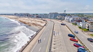 Una strada costiera con accesso alla spiaggia, auto parcheggiate a lato e edifici sullo sfondo.