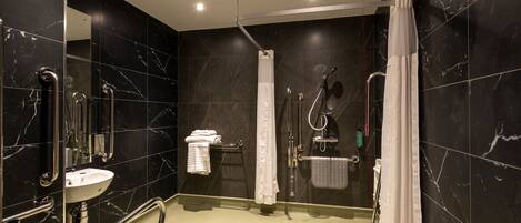 Un baño moderno con pared de mármol negro, un lavamanos blanco, una ducha con puerta de vidrio y una barra de apoyo.