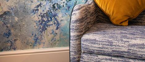 Quarto com parede texturizada e poltrona estampada com almofada amarela.
